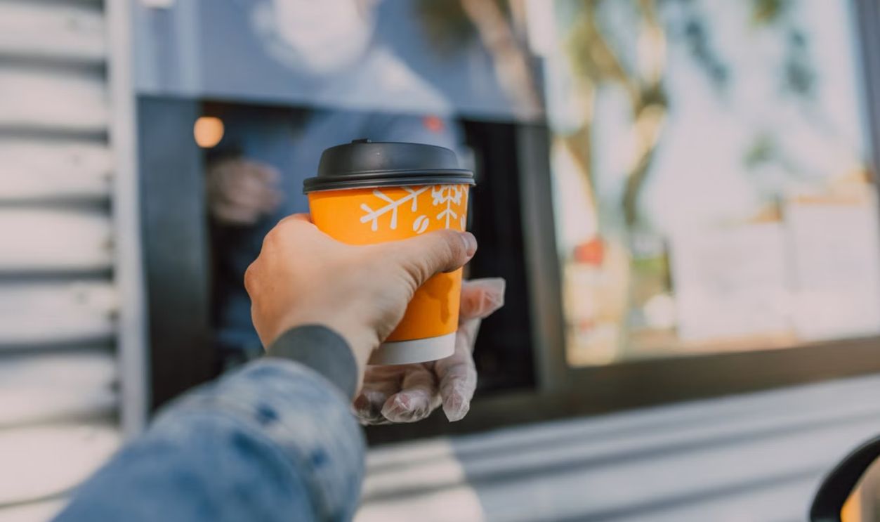 Hand reaching out for a hot coffee cup at a drive-thru window, depicting everyday convenience.
