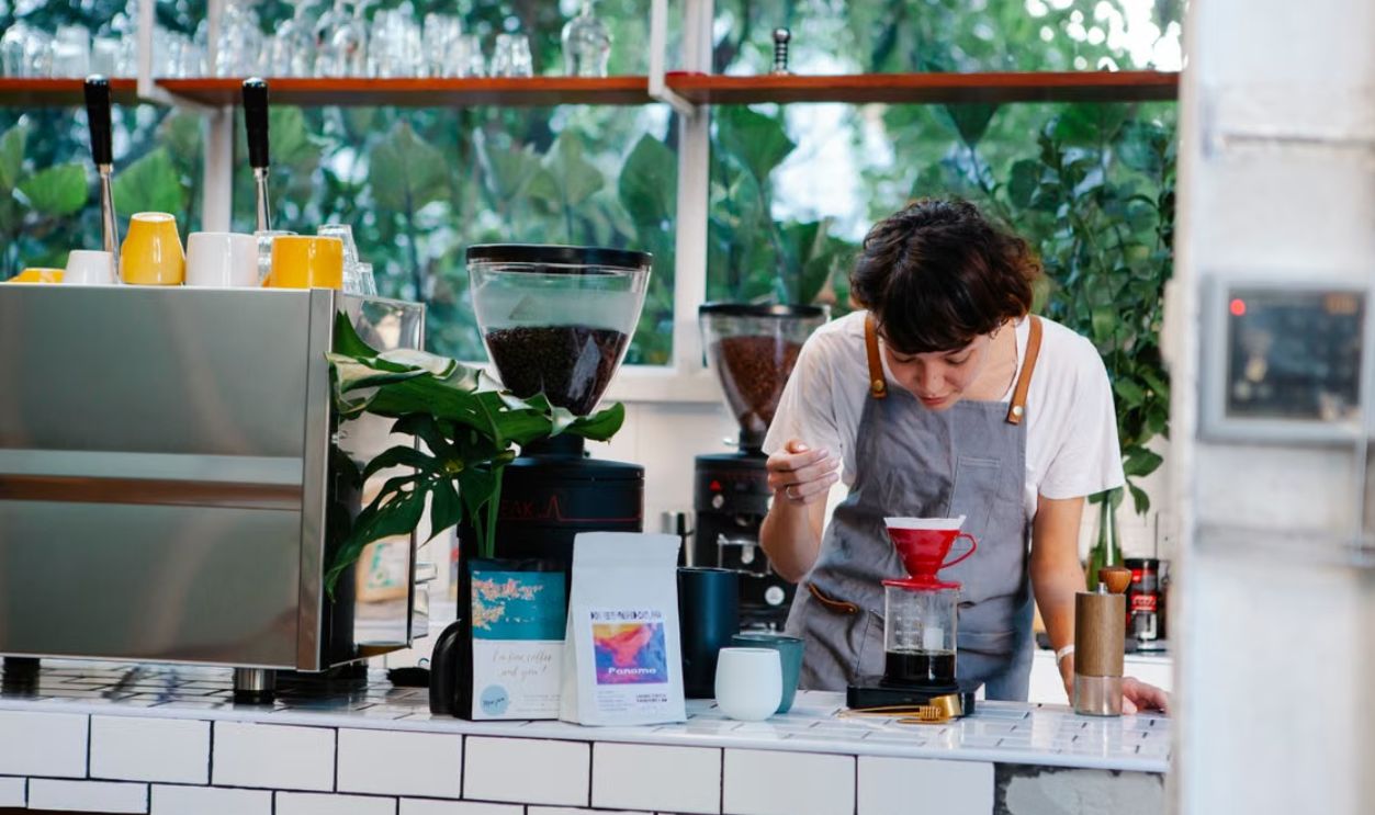 A barista concentrating on preparing pour over coffee in a cozy cafe environment.