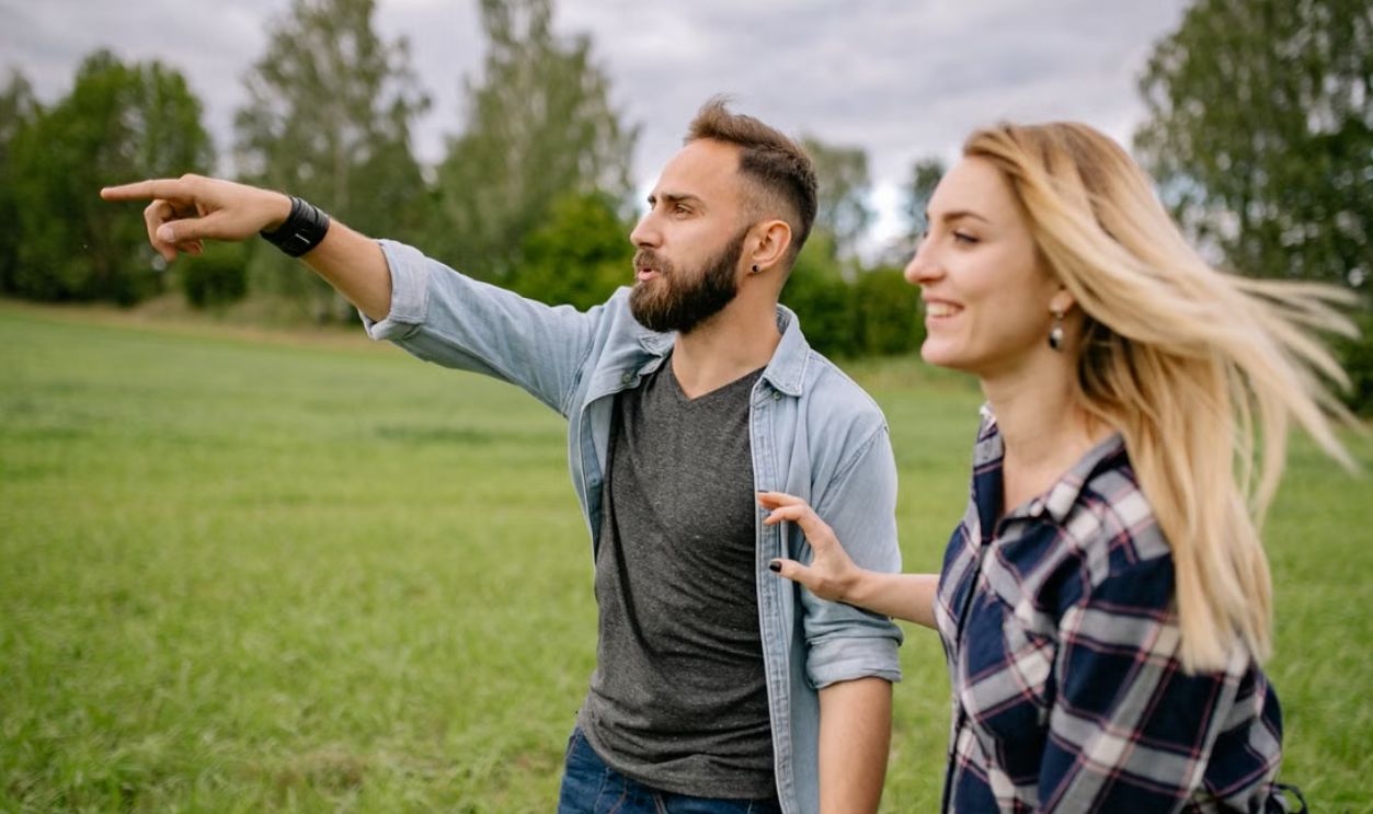 A joyful young couple enjoying a day outdoors, pointing and exploring a green field
