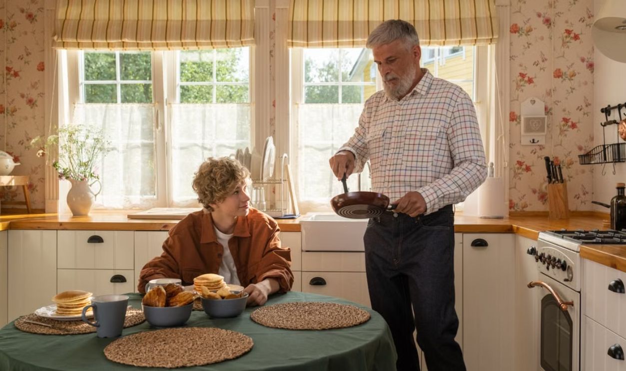 A senior man and teenage boy in a cozy kitchen enjoying pancakes and conversation