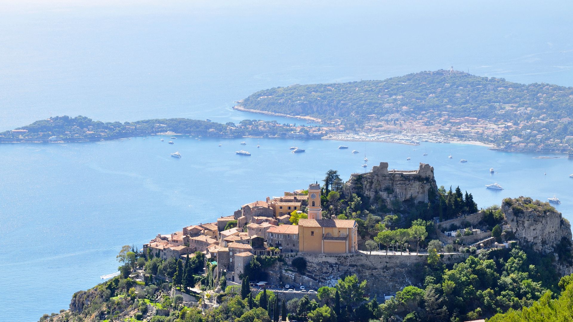 The village of Èze, with its church “Our Lady of Assumption” (Notre-Dame de l’Assomption) and its castle in the foreground, and the Cape Ferrat in the background.