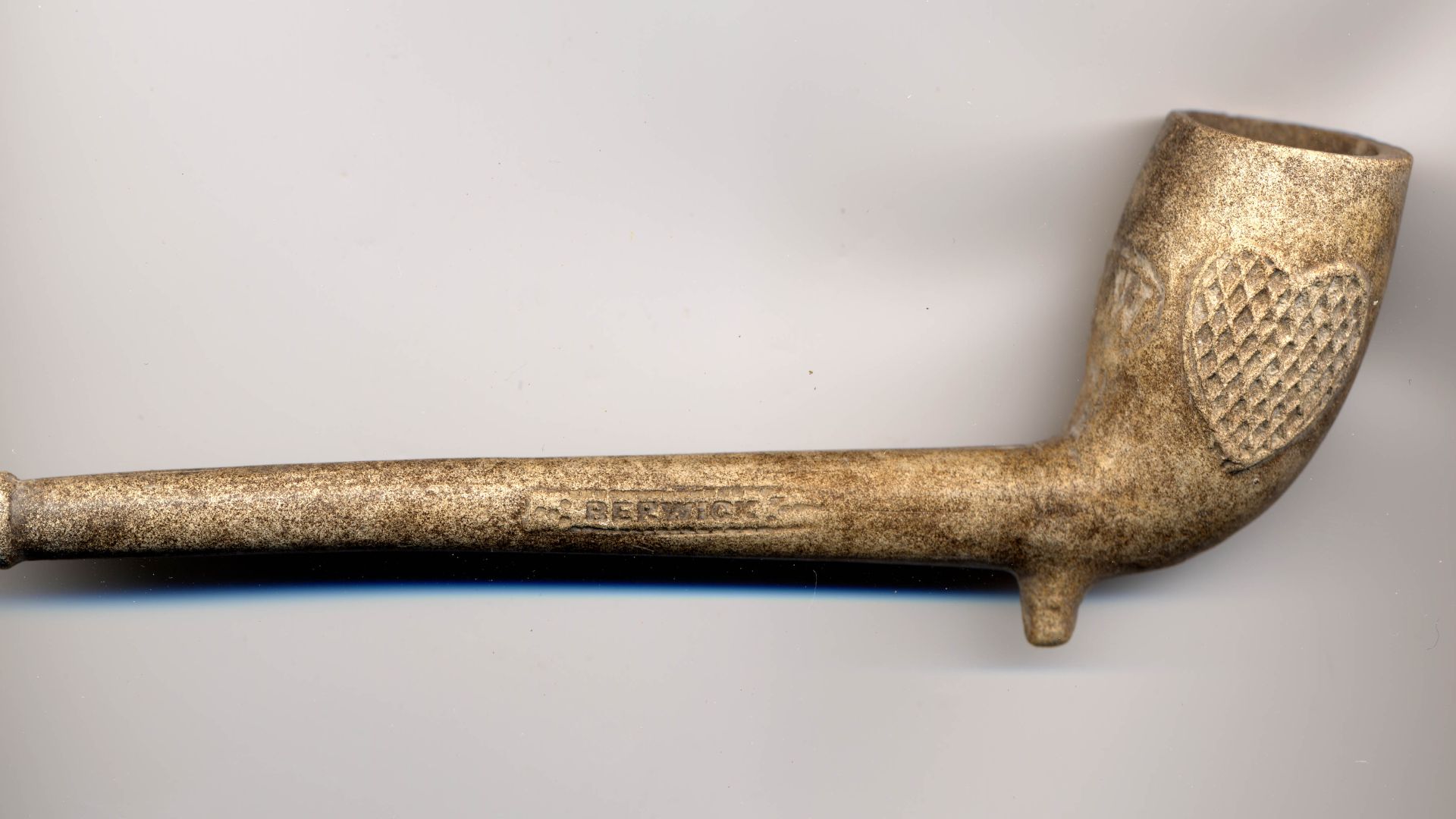 A white pipe clay tobacco pipe, dating to the mid nineteenth century. The pipe is complete and does not appear to have been used. The stem is stamped with the words 'TENNANT & SON' and 'BERWICK'. The bowl is stamped with the initials 'TW' within an oval d