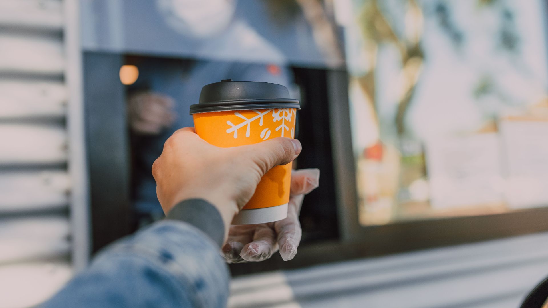 Hand reaching out for a hot coffee cup at a drive-thru window, depicting everyday convenience.