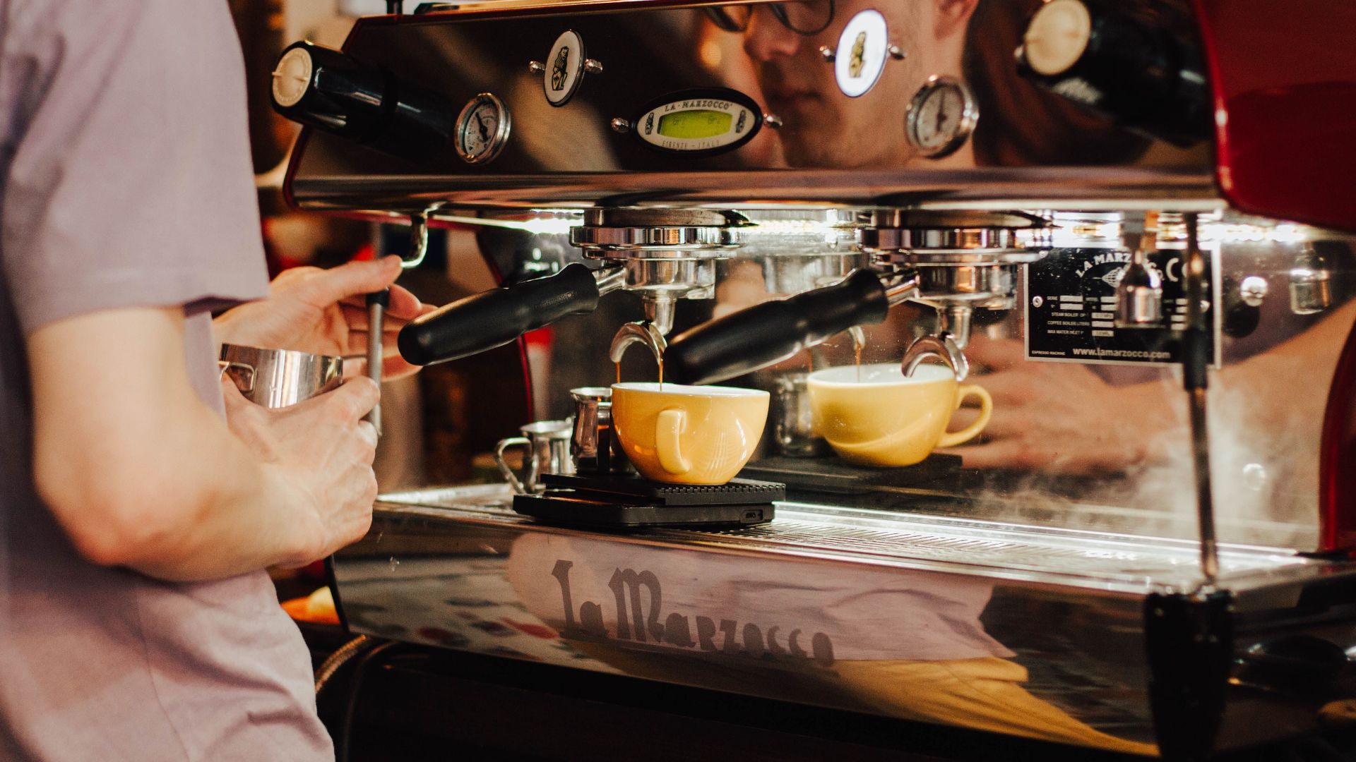 Barista using espresso machine to brew coffee in a café, showcasing coffee preparation process.