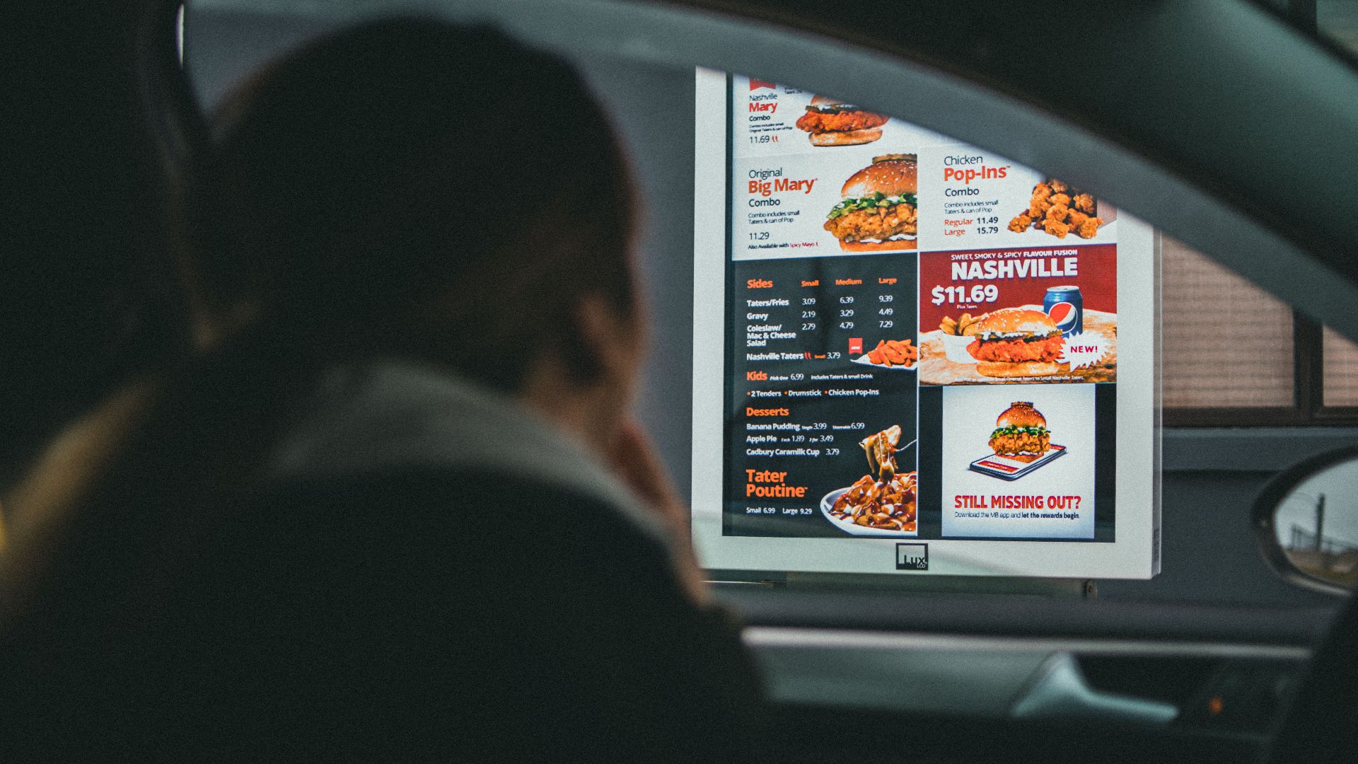 A woman in a car views the menu at a fast food drive-thru, ready to order her meal.