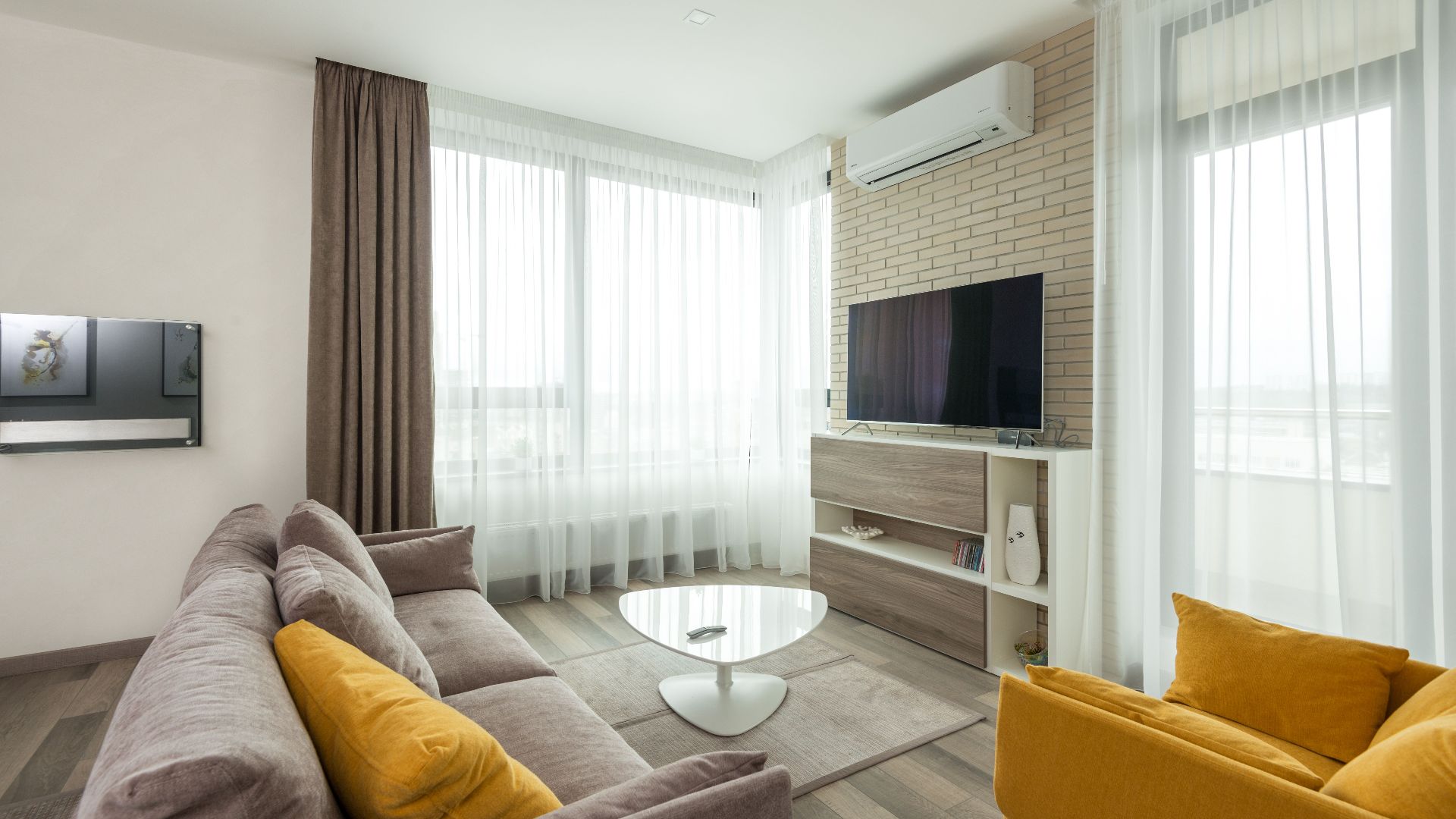 Soft comfortable sofa with cushions and armchair placed in front of TV hanging on brick wall in spacious living room of modern apartment