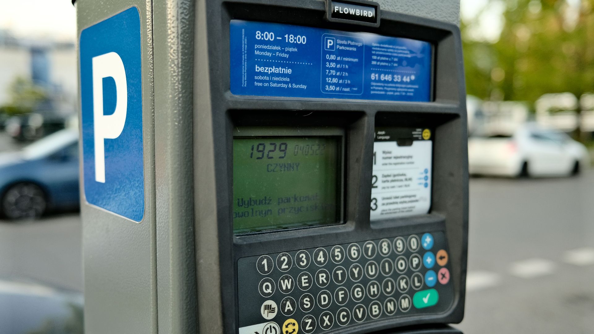 Close-up of a digital parking meter in a city setting with cars in the background.