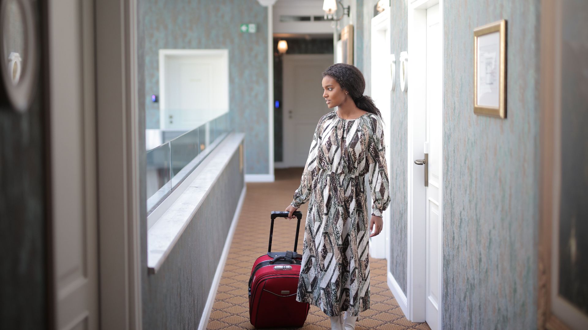 A woman walks with luggage through a stylish hotel corridor, embodying travel elegance.