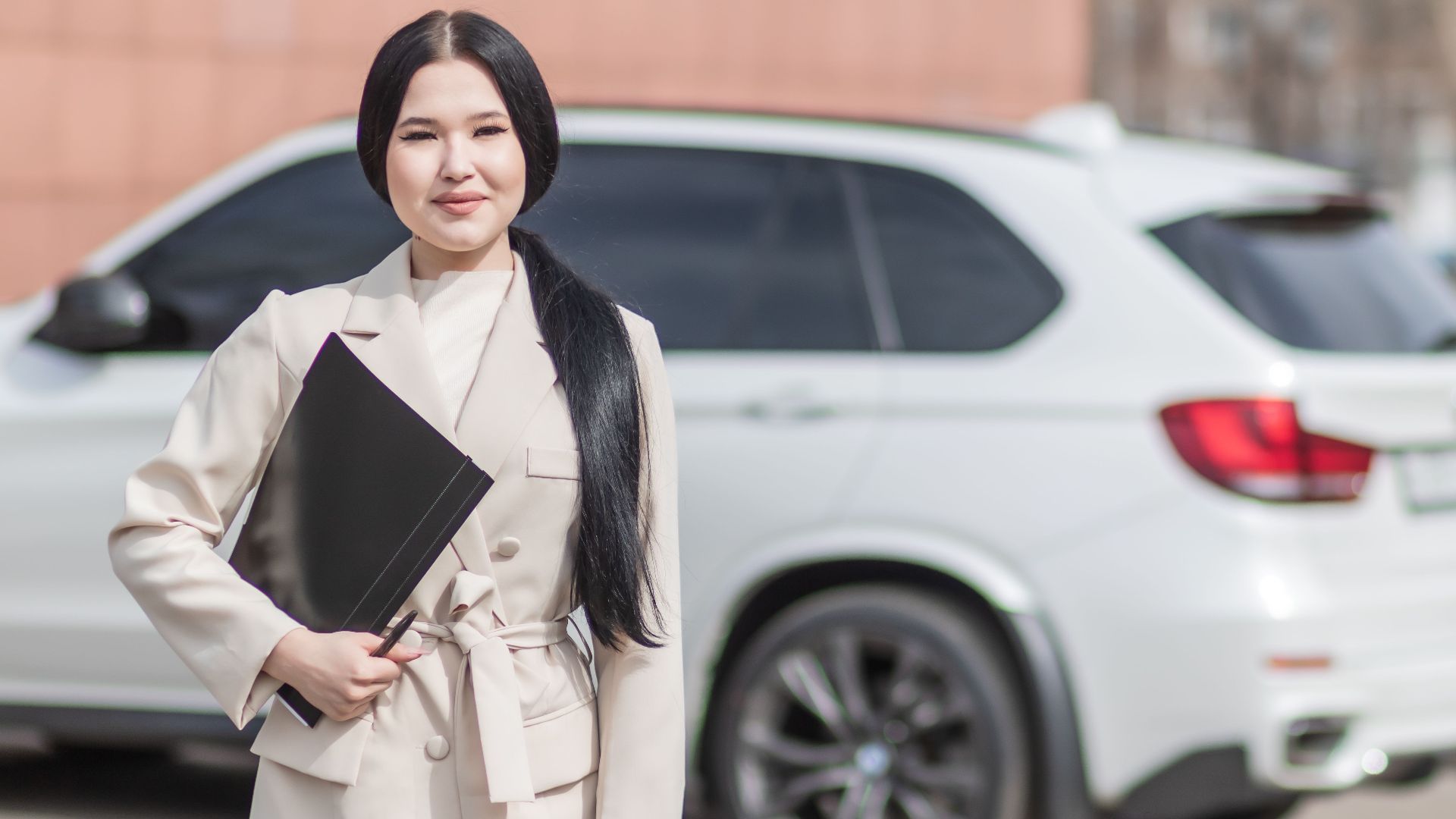 Smiling professional woman standing confidently by a luxury car, embodying success.