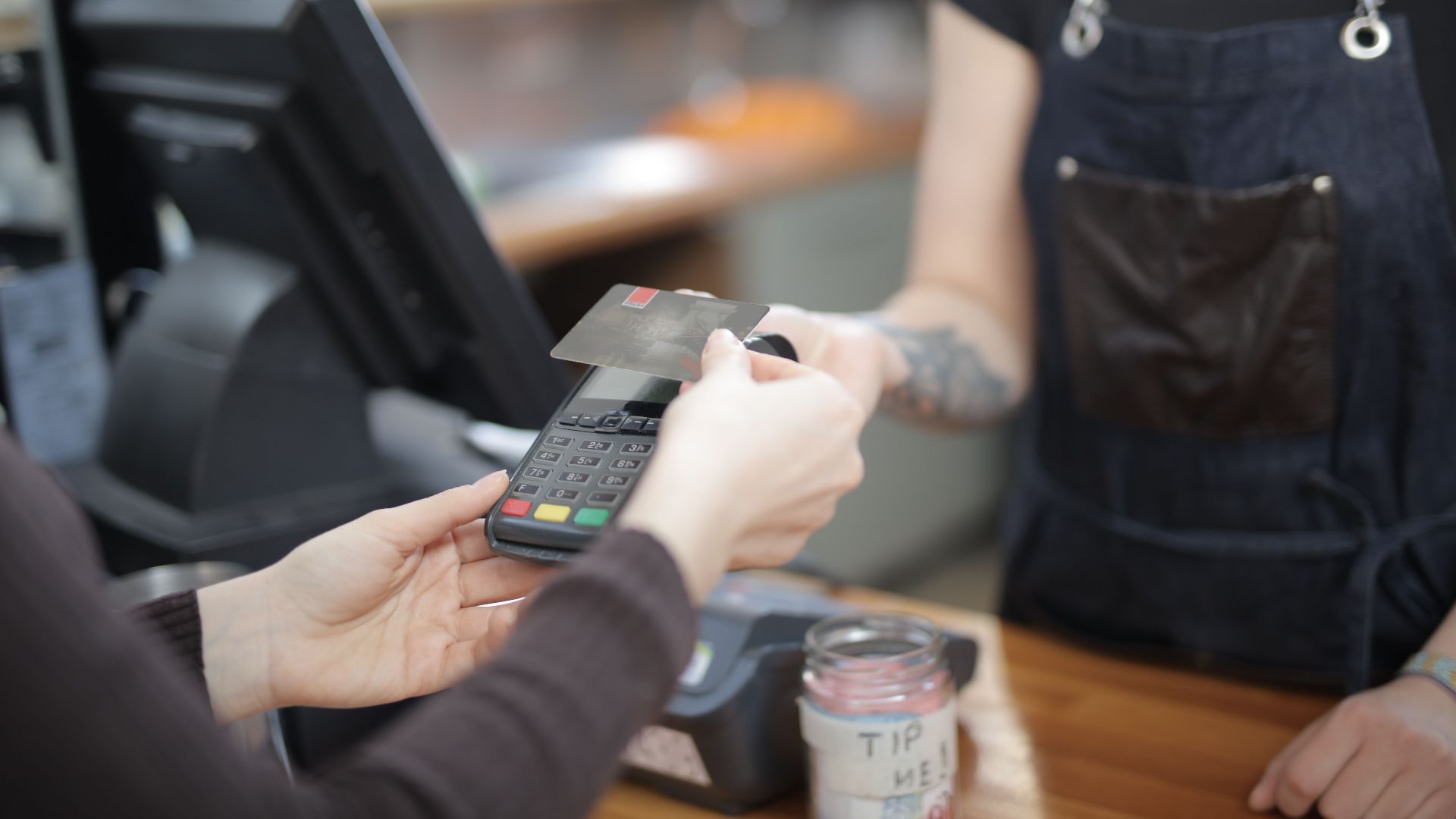 Close-up of customer and cashier during a credit card transaction at a store counter indoors.