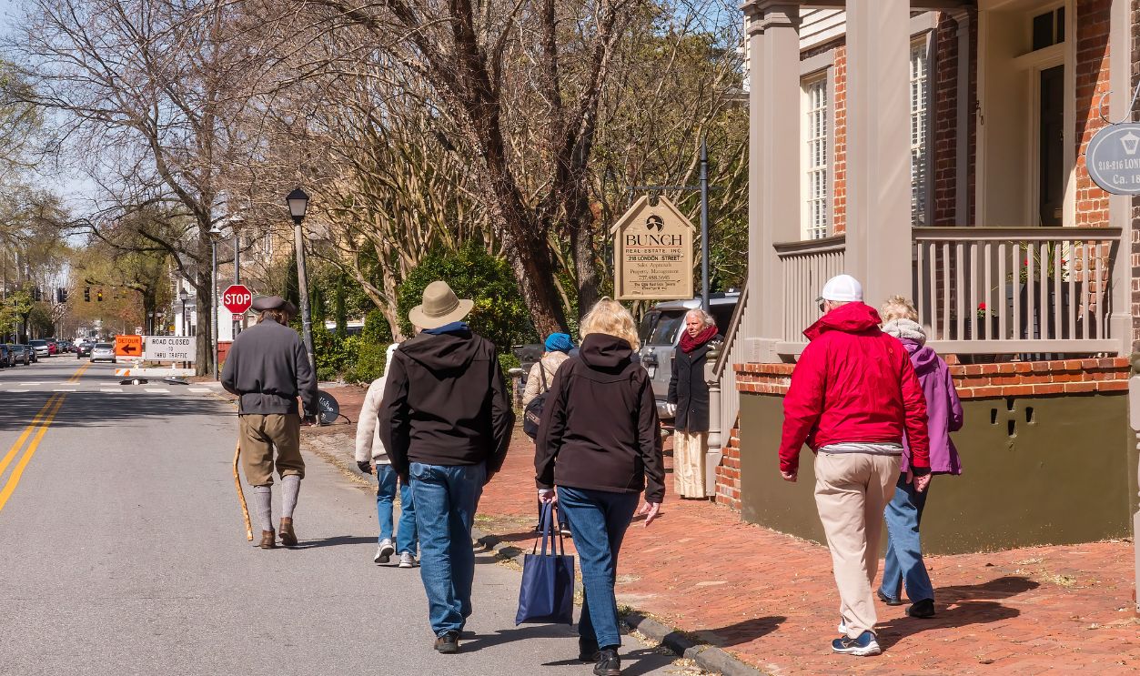 PORTSMOUTH, VA, USA - MARCH 29, 2022: Senior sightseers follow a guide in period costume on a walking tour near an intersection of an historic district of town on a chilly morning in spring.