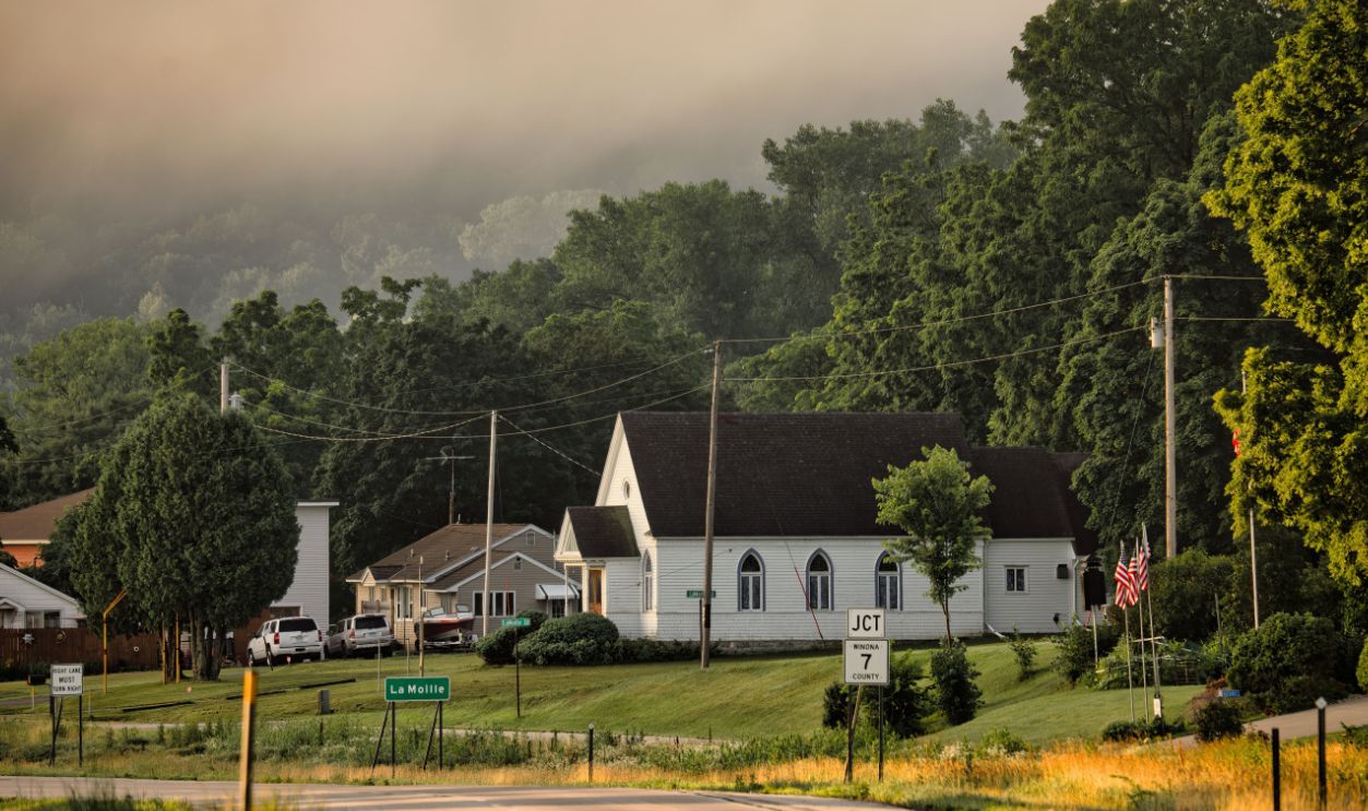 A foggy morning scene in Dakota, MN showcasing a quaint small town with green trees and classic architecture