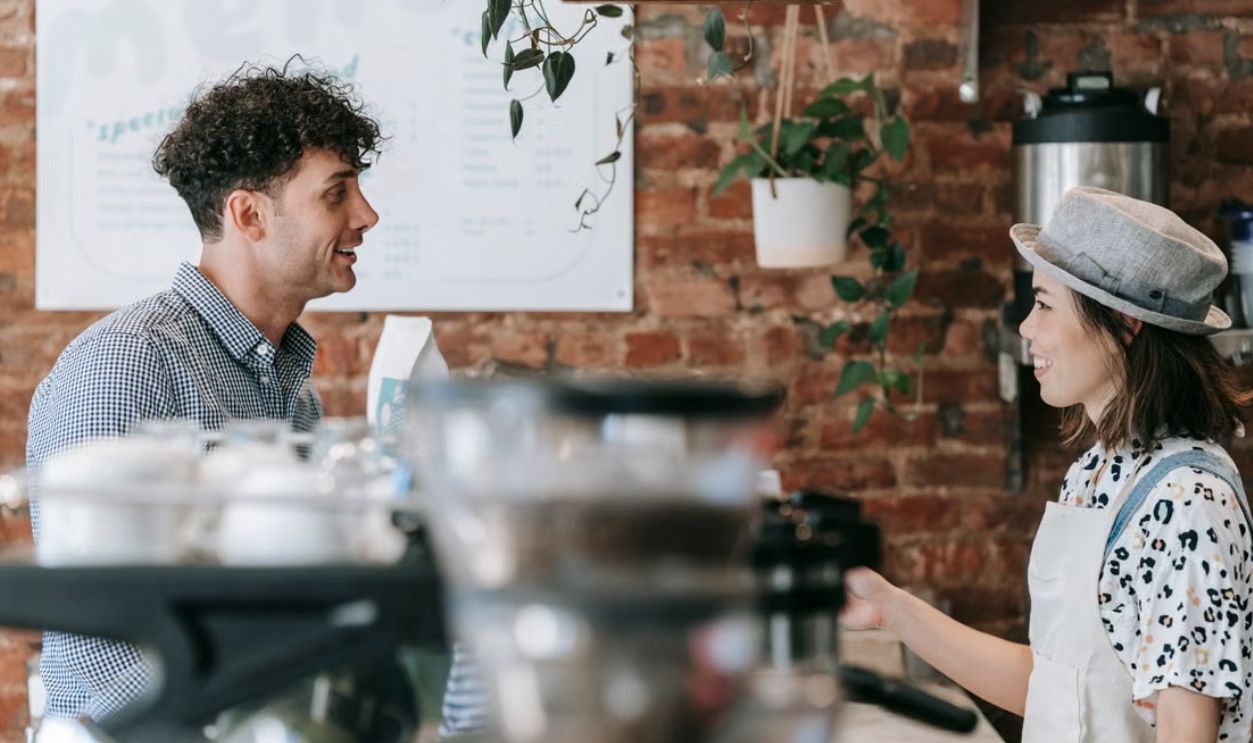 Smiling barista engaging in conversation with a customer in a cozy coffee shop