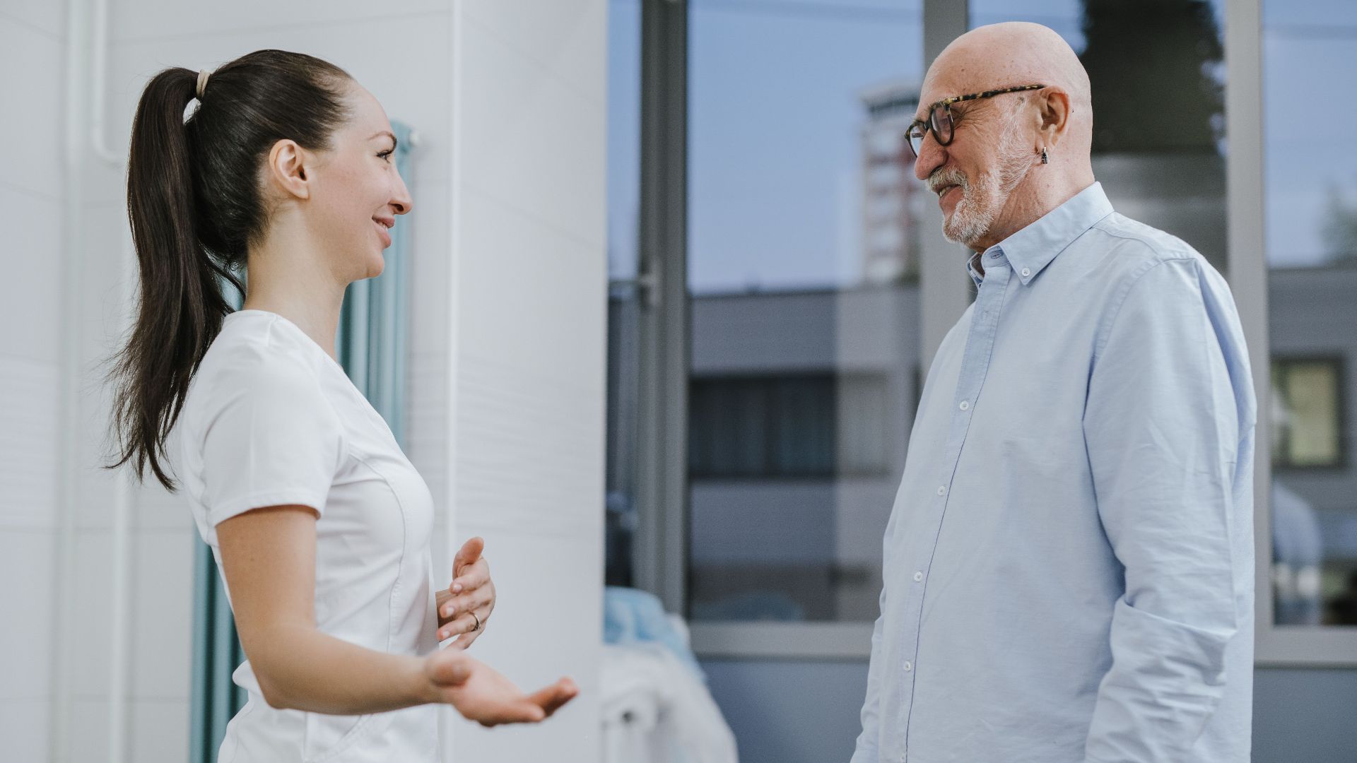 A nurse and senior patient share a light moment during a healthcare appointment indoors.