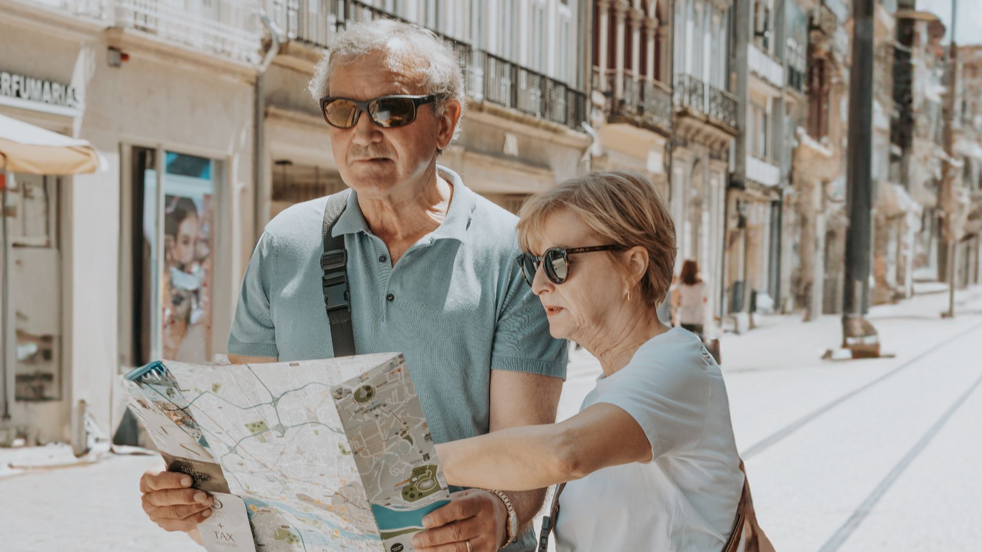 Senior couple in summer attire navigates with a map on a sunny Porto street.