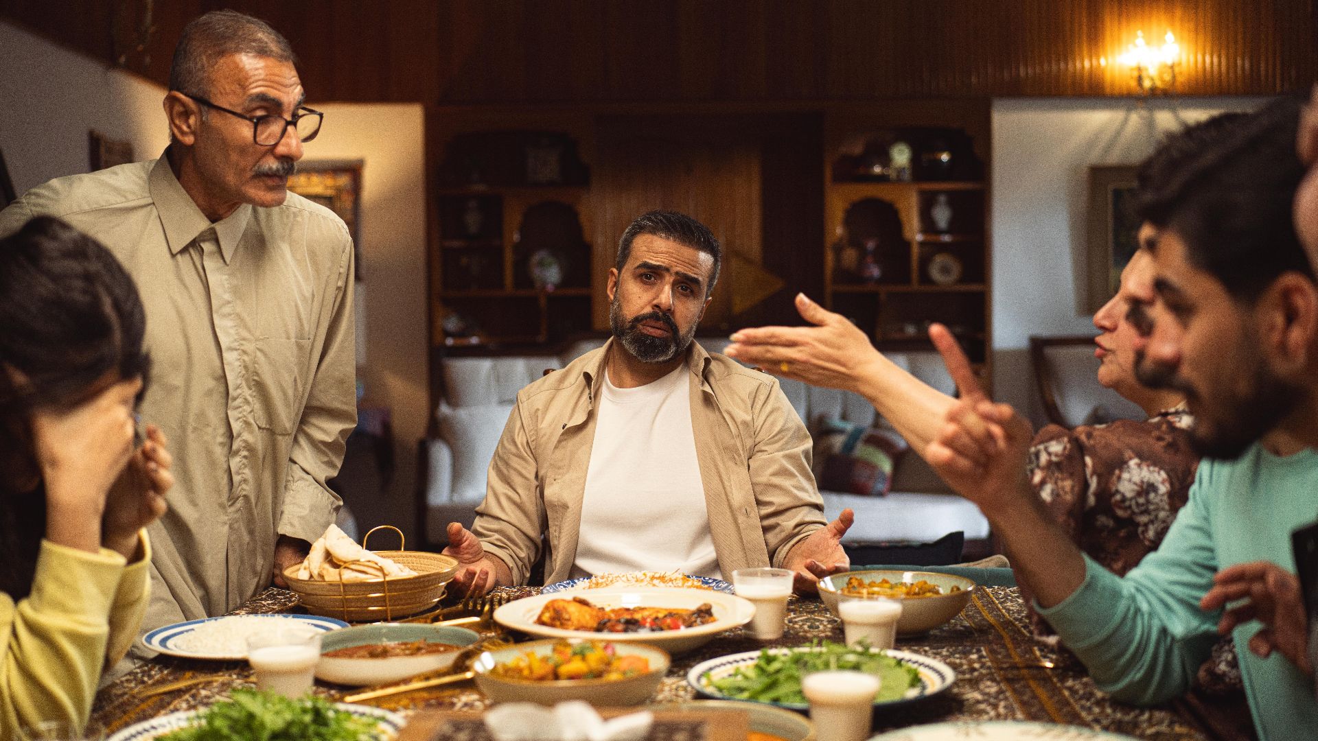 A family engages in a lively discussion around a dinner table filled with dishes.