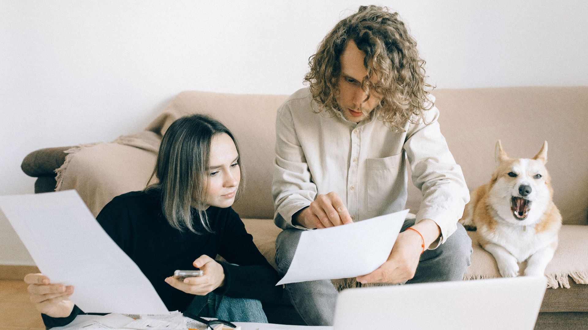 A couple working remotely at home with documents and a dog on the sofa.