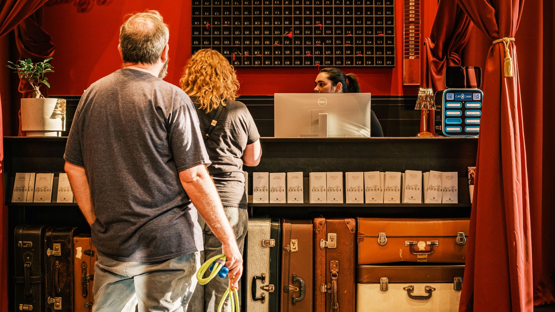 A couple with a dog checks in at a stylish, vintage hotel front desk.