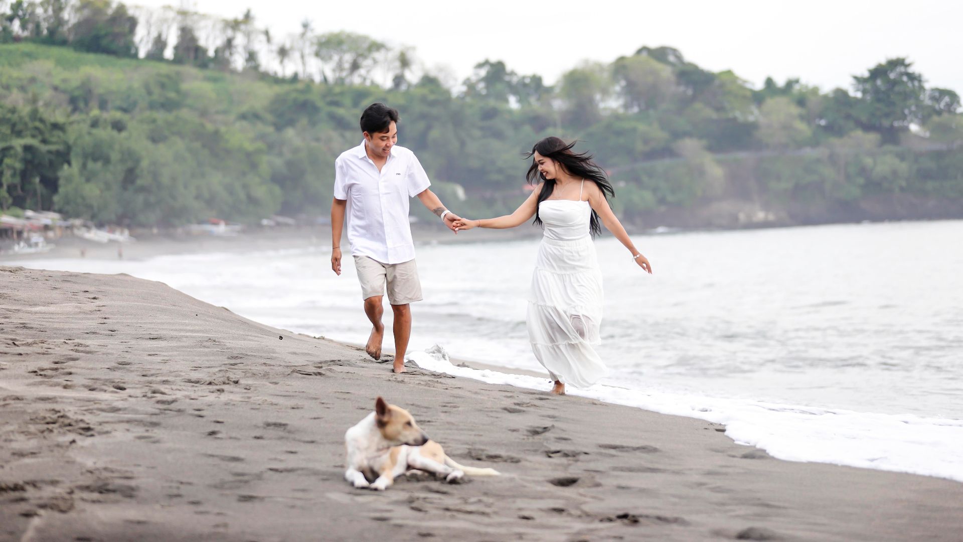 Couple joyfully walking on the beach with a dog in Nusa Tenggara Barat, Indonesia.