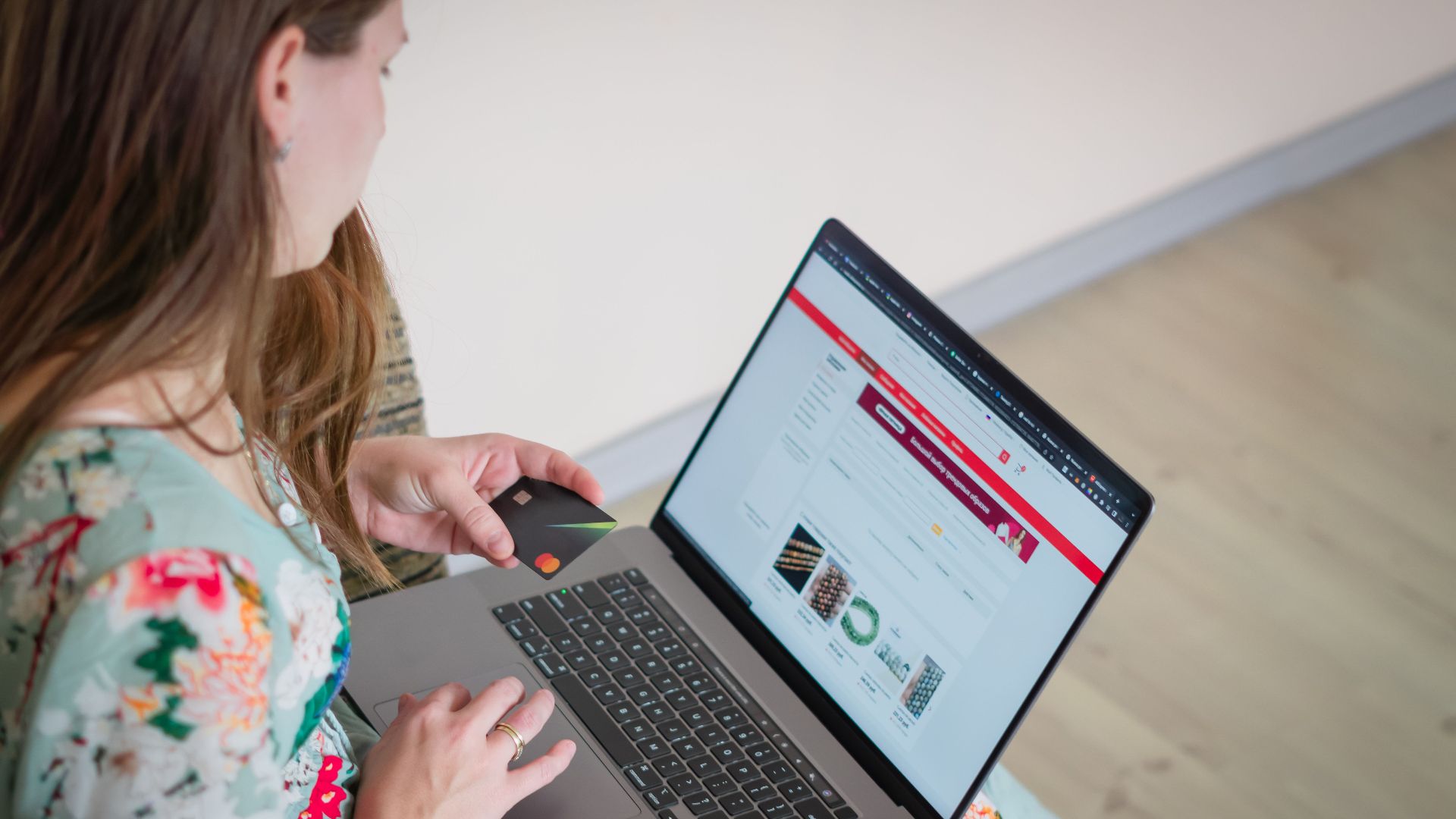 Woman in floral dress shopping online with a laptop and credit card indoors.