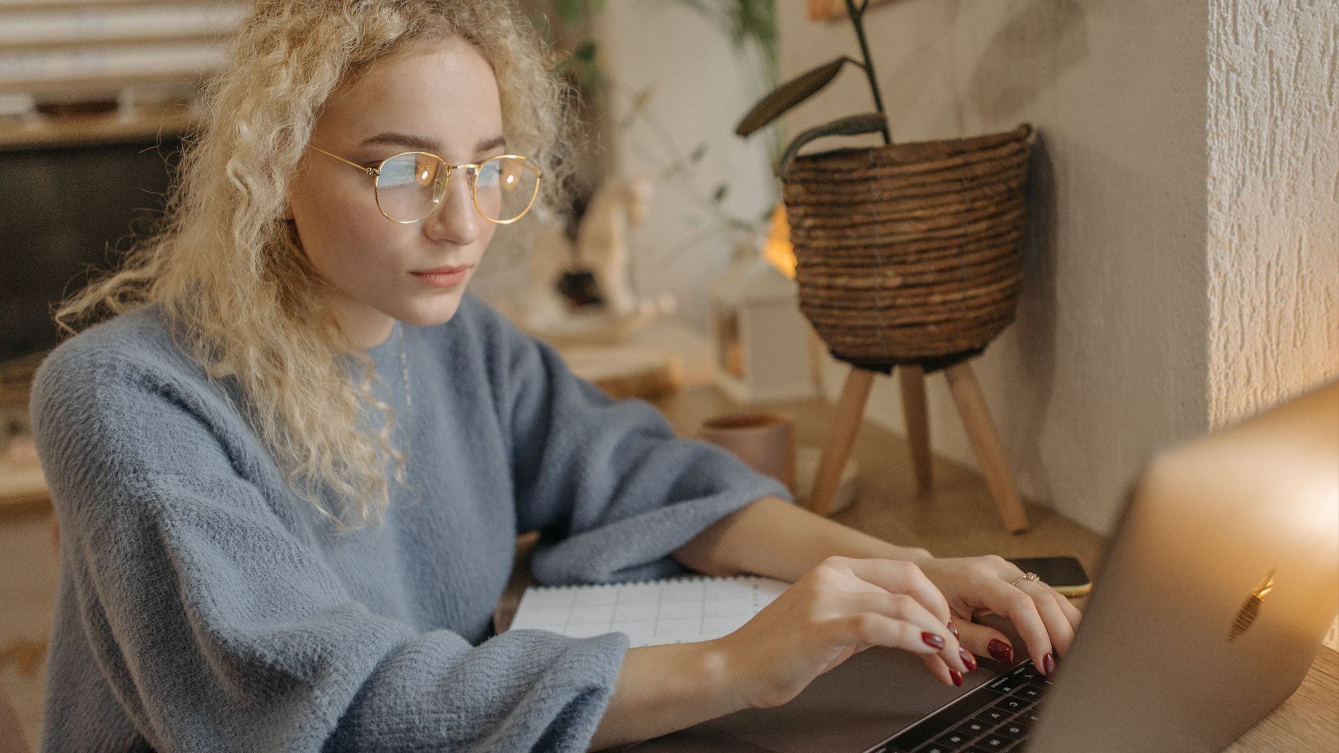 Focused young woman with curly hair working on her laptop in a cozy home office setting.