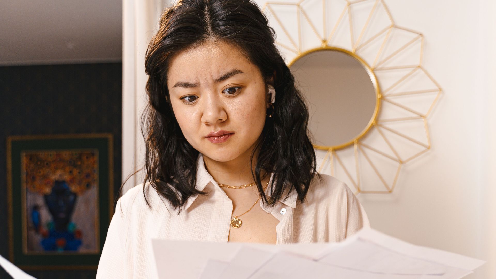 Young woman looks confused while reviewing documents in a modern home interior.