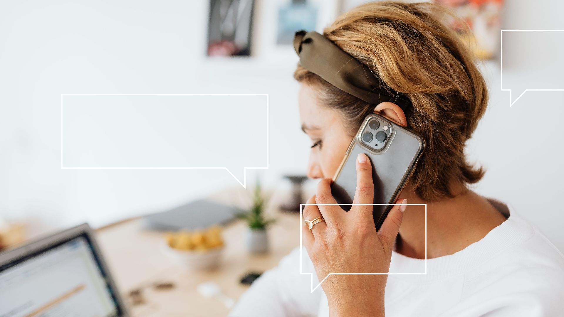 A woman multitasking, on a phone call while working from home with a laptop.