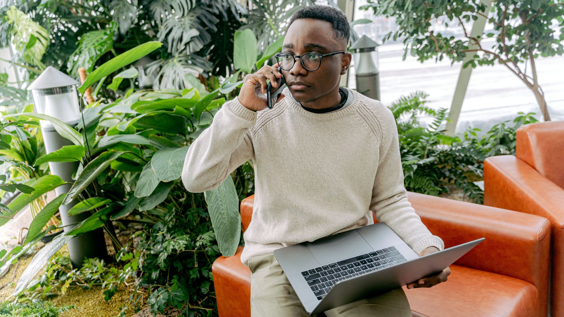 Focused young man in a cozy indoor setting multitasking with phone and laptop.