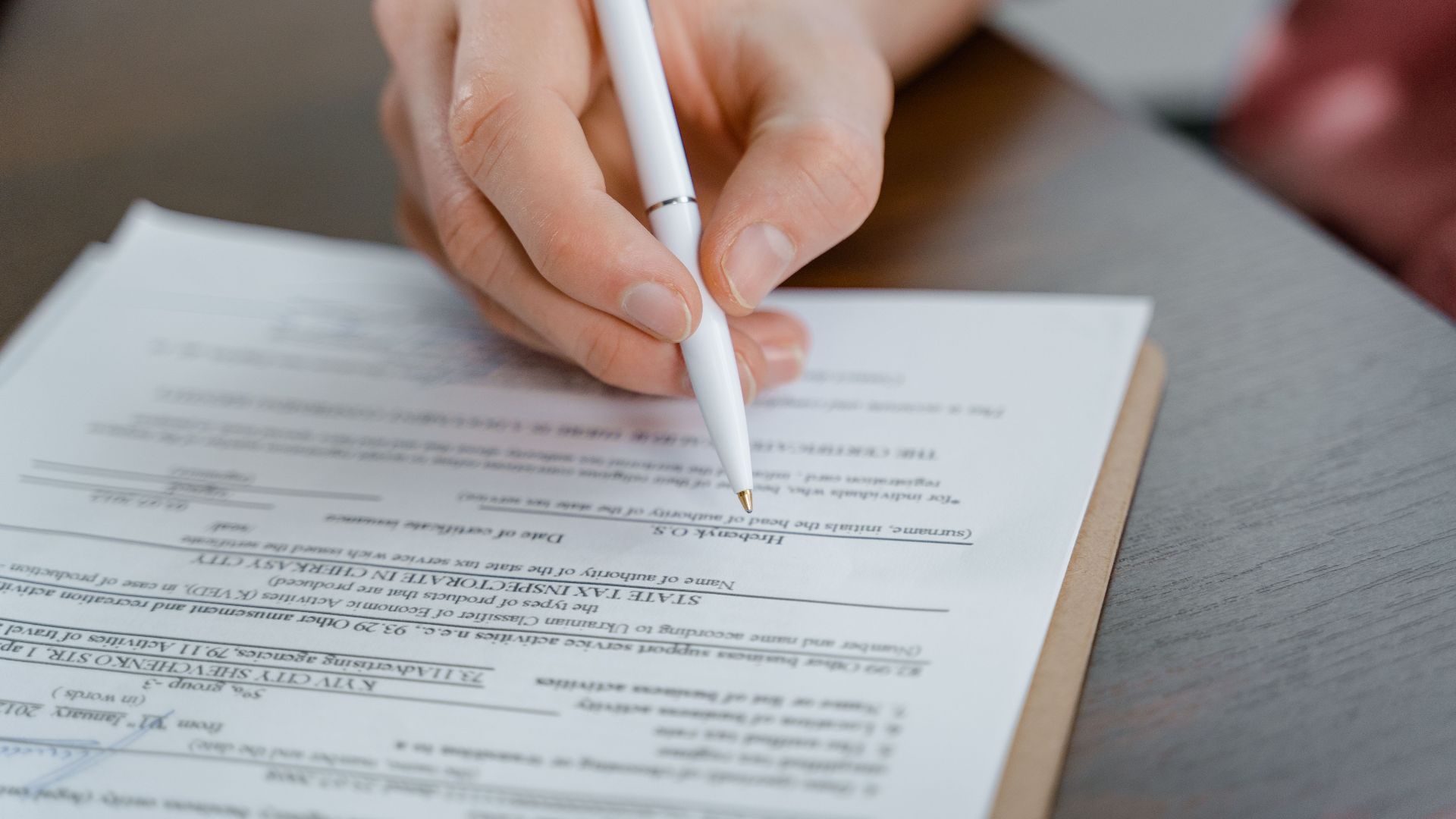 A hand holding a pen signing a document, close-up shot with focus on the paper.
