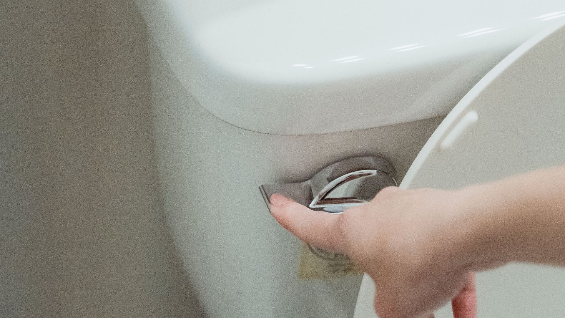 Close-up of a hand flushing a modern toilet, emphasizing hygiene and water conservation.