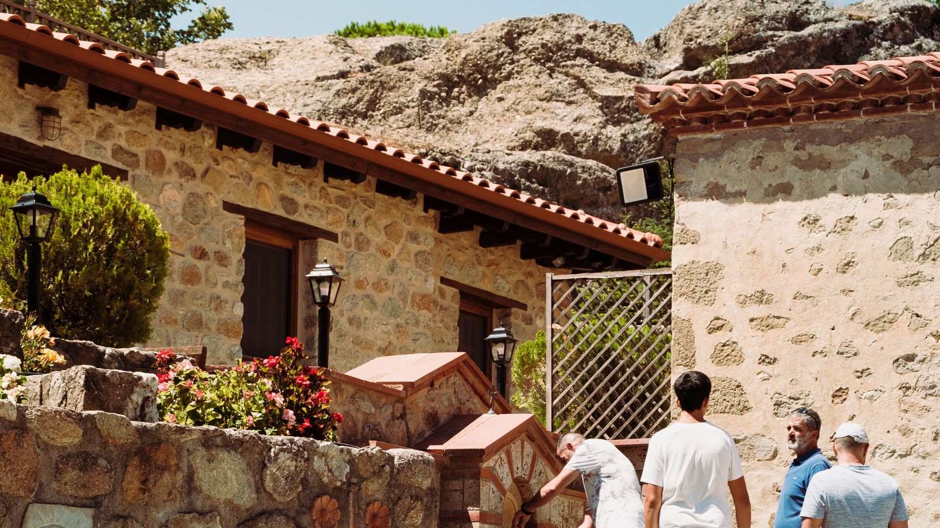 Tourists exploring traditional stone architecture in a Greek village under clear blue skies.