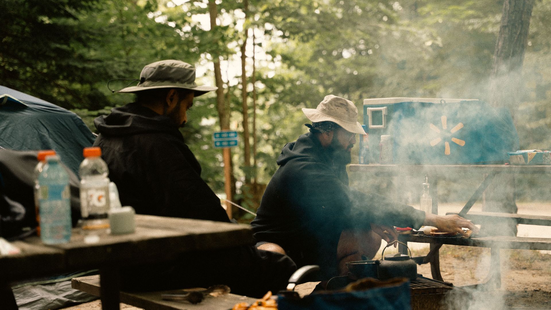 Outdoor camping scene with men cooking at a campsite with tents and trees.
