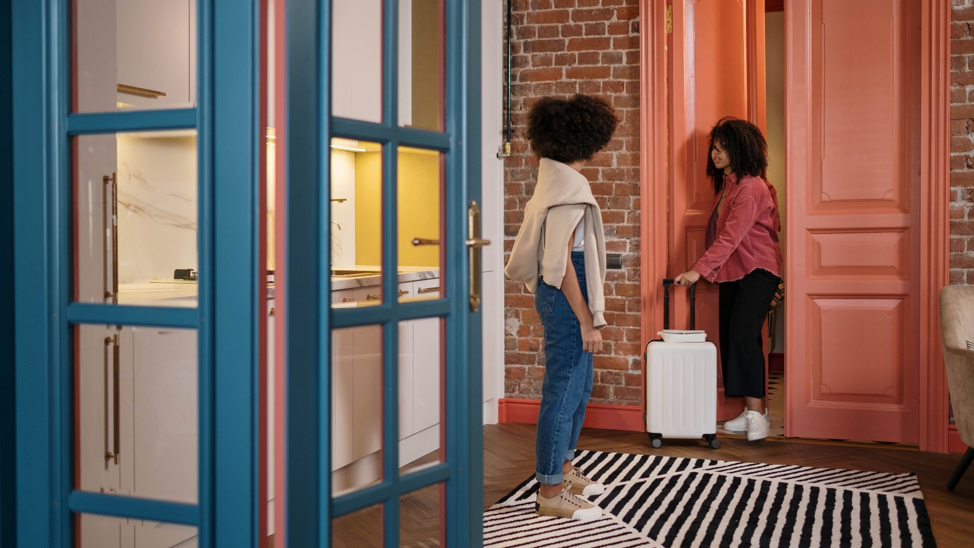 Two women with luggage in a stylish apartment hallway, getting ready to travel.