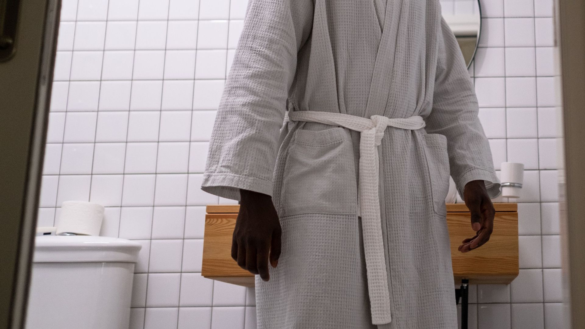 A man in a white bathrobe is looking behind him in a modern restroom with a mirror.