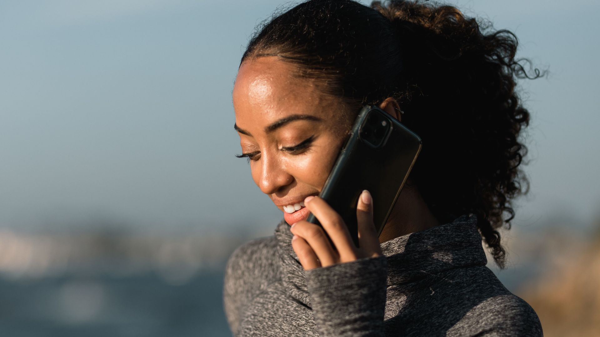 Young woman smiling during a phone call by the sea on a sunny day.