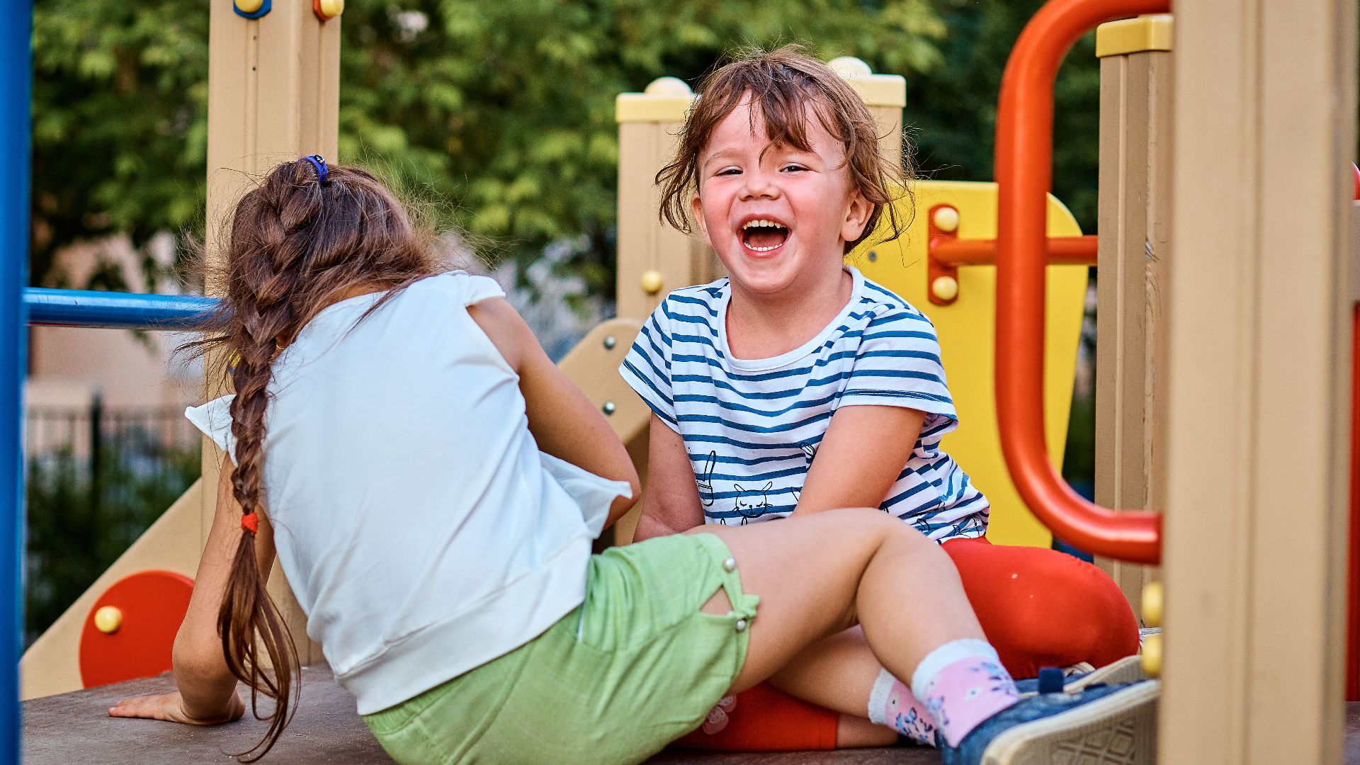 Young girls laughing and playing on an outdoor playground during the day.