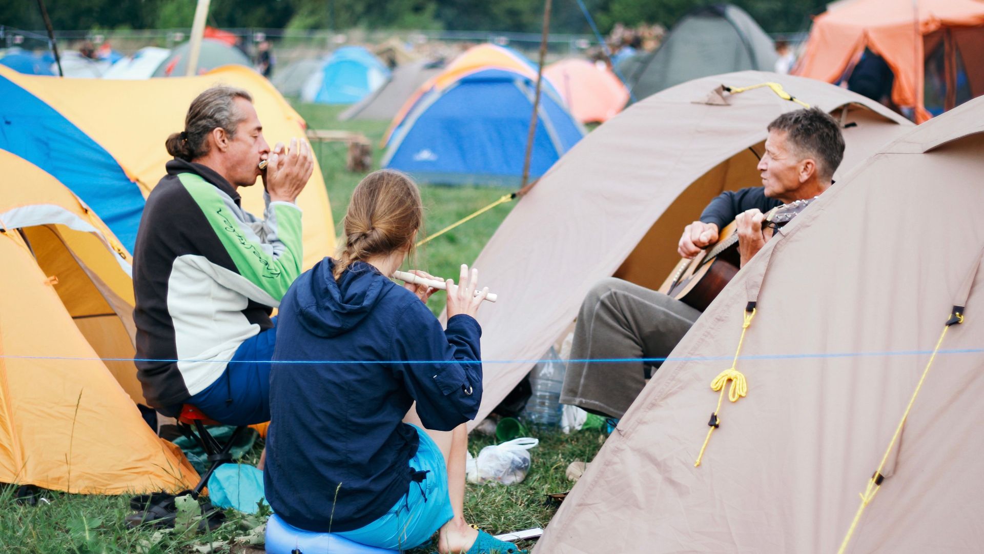 A group of campers playing music and bonding at a campsite outdoors.