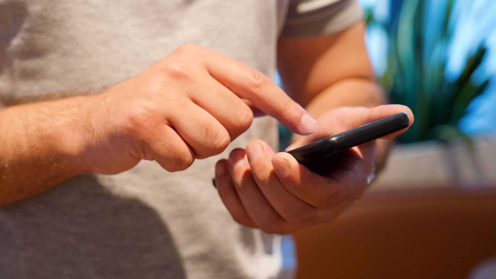 Adult male using smartphone in a bright indoor setting, focusing on the device and interaction.