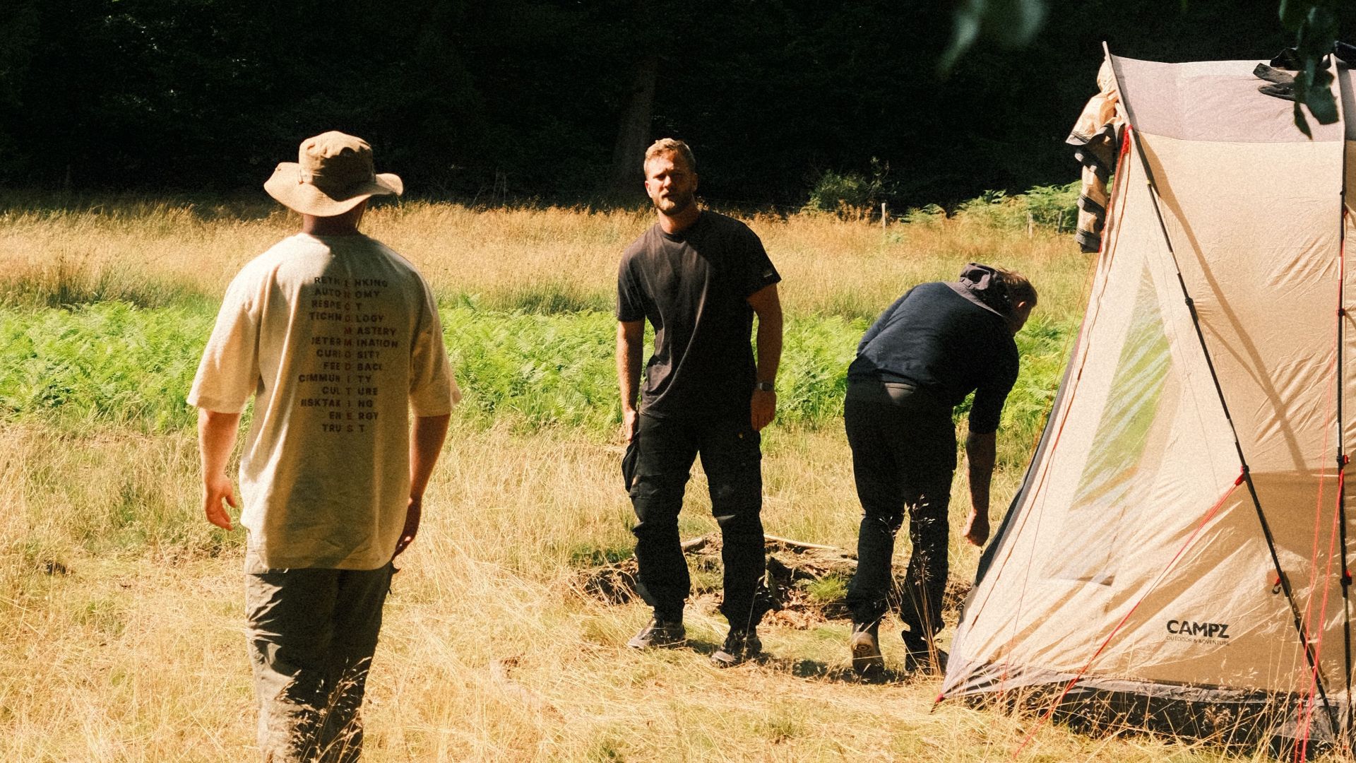 A group of adults setting up a campsite with a tent in a grassy area.