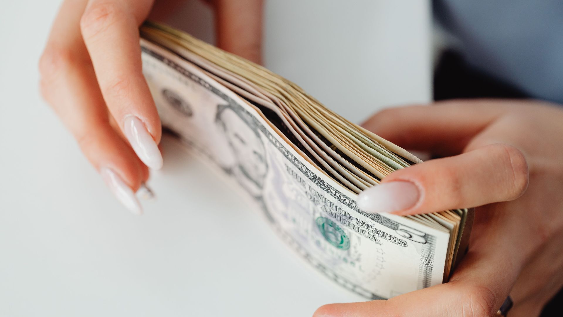 Hands carefully holding a stack of US dollar bills, representing finance and currency.