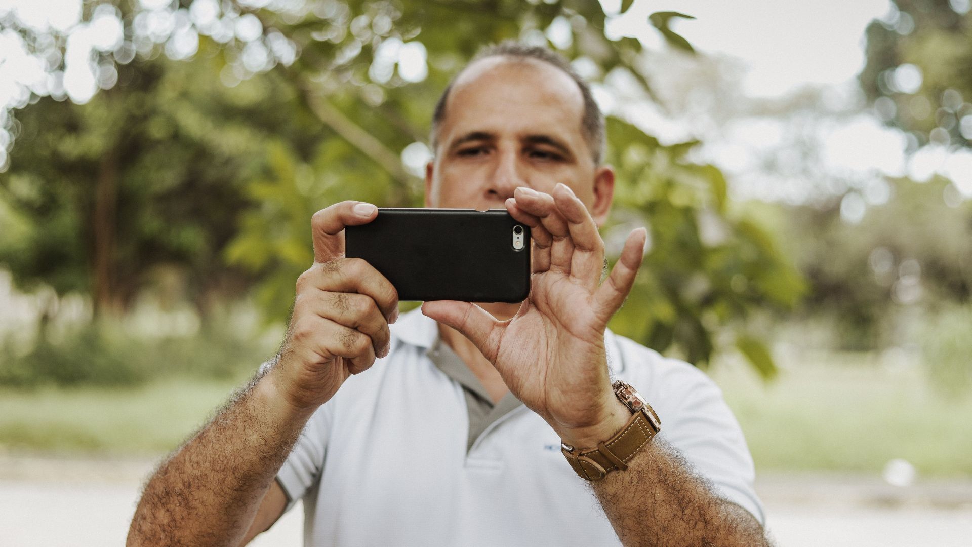 Adult man using smartphone to take a photo in a natural setting, showcasing modern technology and leisure.