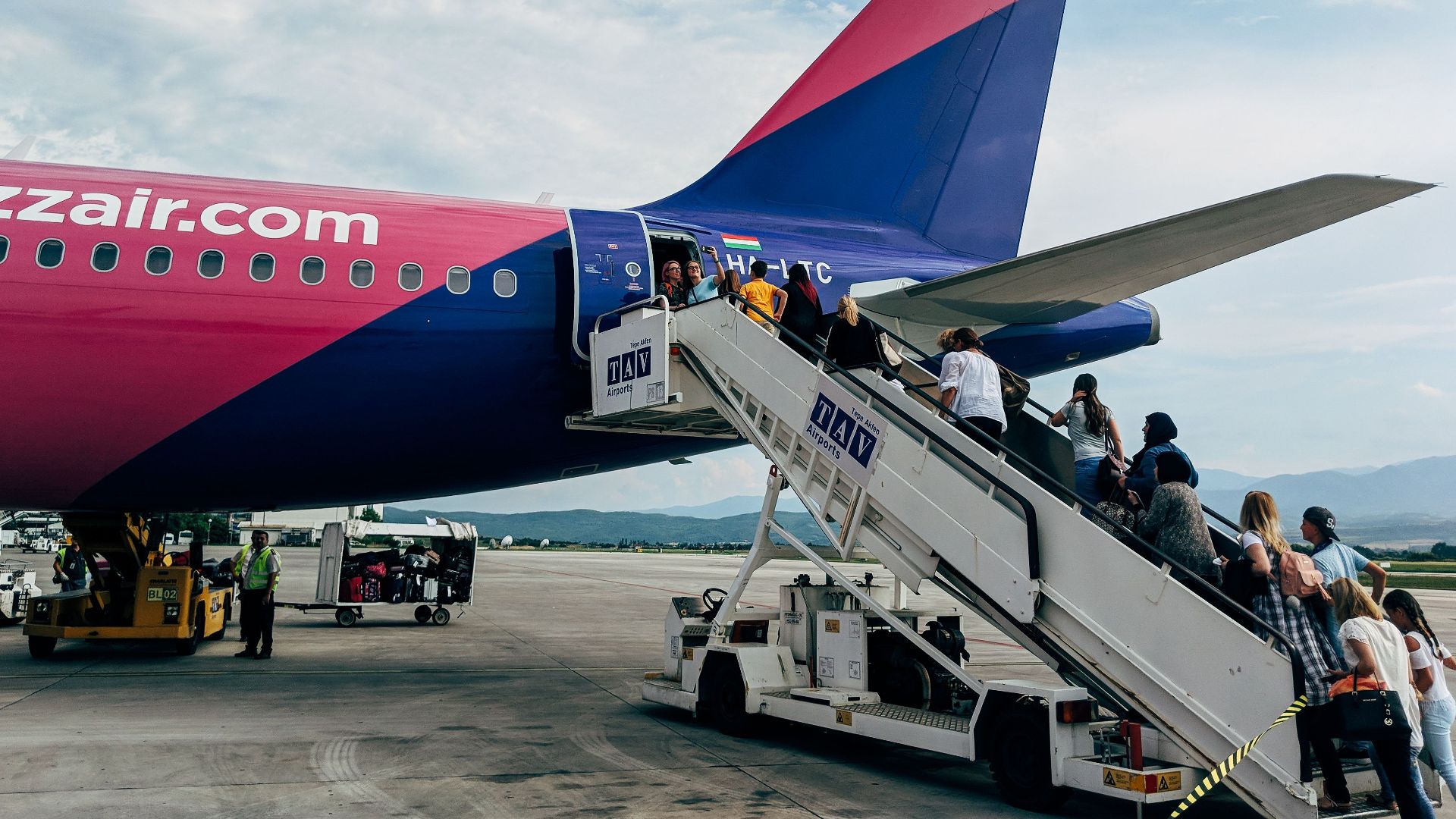Travelers boarding a WizzAir Airbus A320 jet on a clear day at the airport.