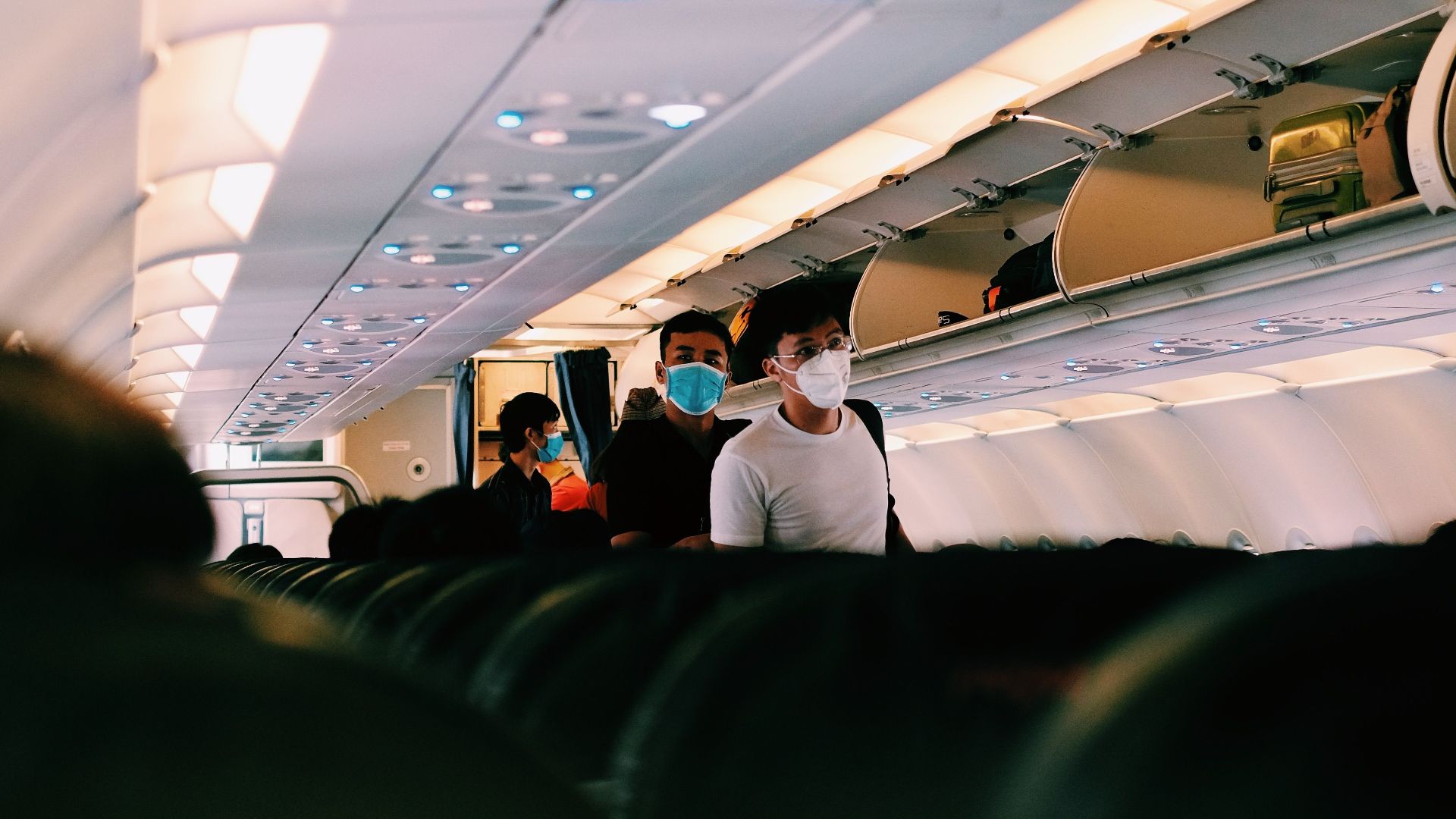 Inside airplane with passengers wearing face masks walking through the aisle.