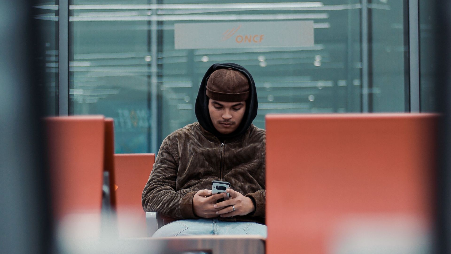 Young man sitting in an airport lounge in Rabat, Morocco, using a smartphone. Modern and relaxed setting.