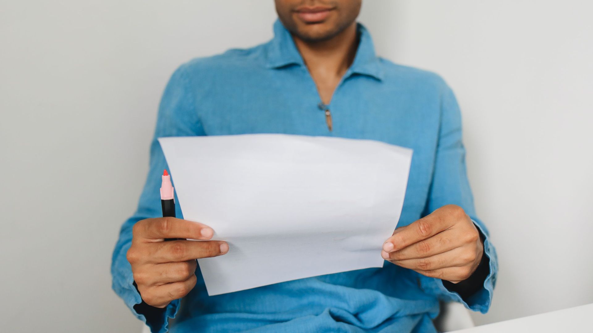 Close-up of a man holding and examining a paper with a pen indoors.