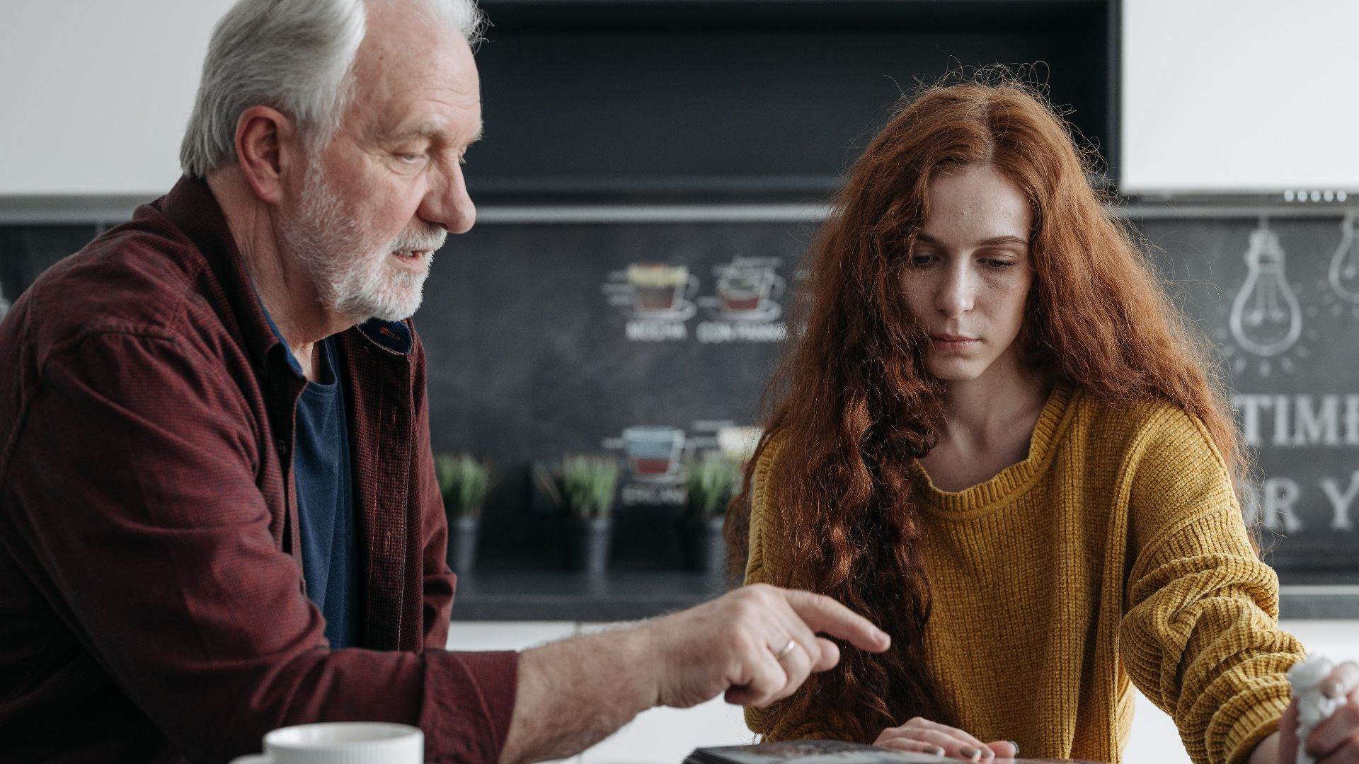 Elderly man and young woman share a poignant moment reminiscing over a photo album.