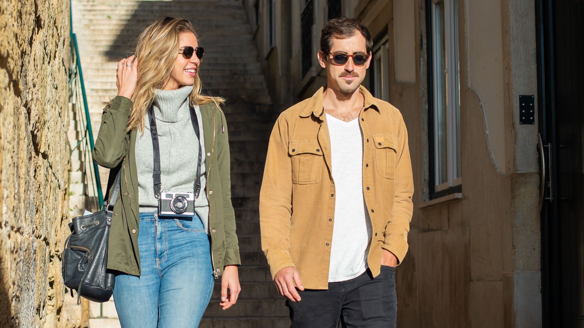 A happy couple walking down a sunlit narrow street during their travel adventure.