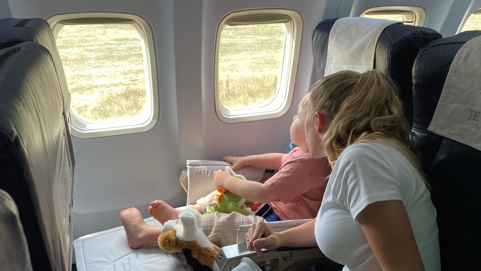 Mother and child sitting inside airplane, enjoying scenic view through windows during flight travel.