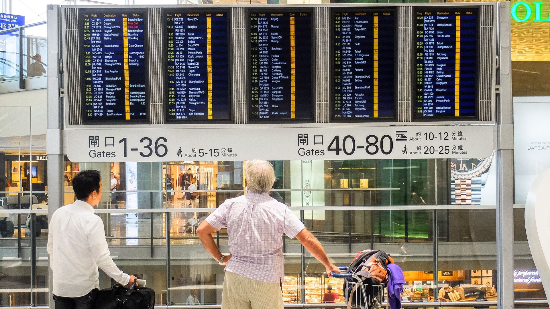 Passengers review flight information on a digital board in Hong Kong airport terminal.