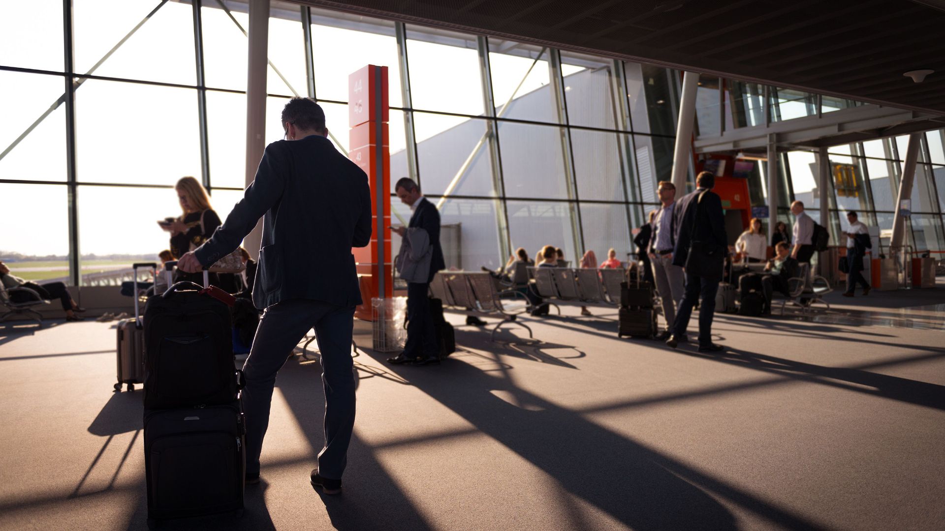 Travelers in a bustling airport terminal with carry-on luggage waiting for departure.